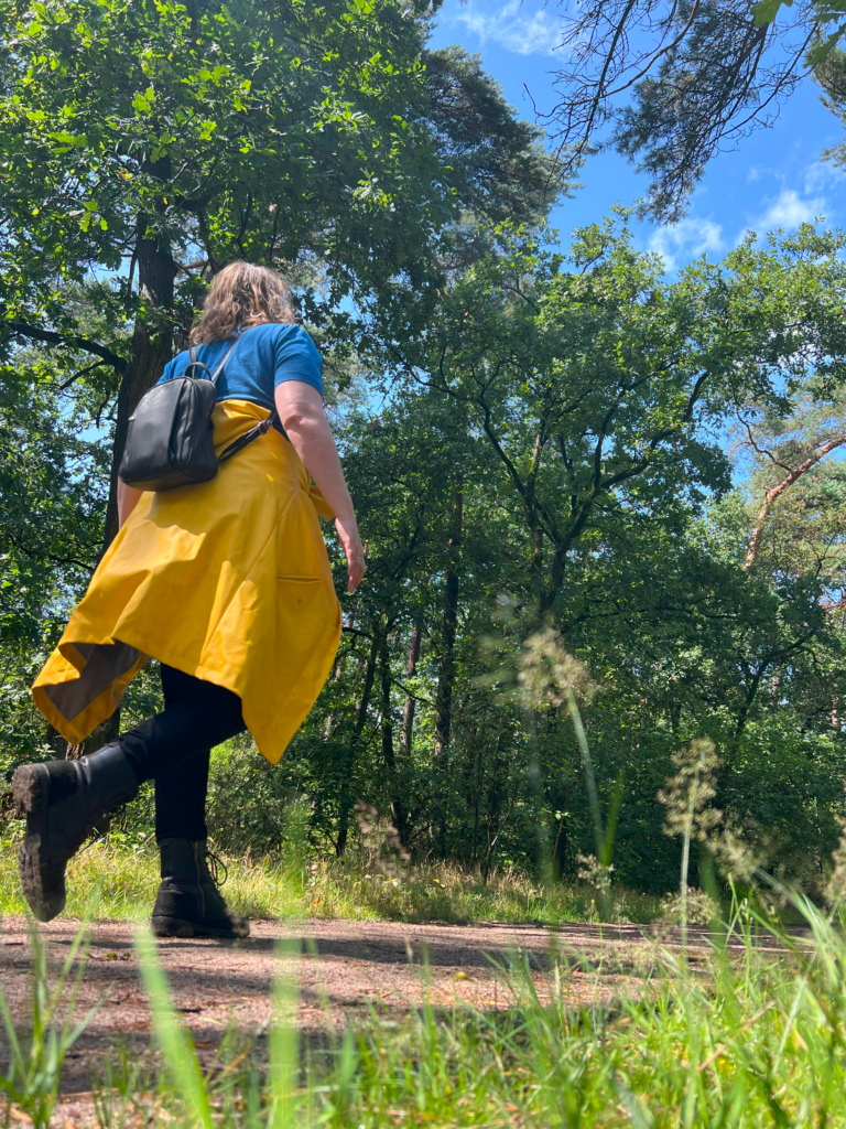 Een foto van Margaret wandelend in het bos, met haar regenjas om haar middel gebonden.